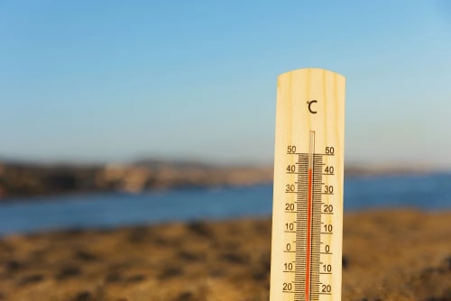 Termómetro marcando alta temperatura en un paisaje costero