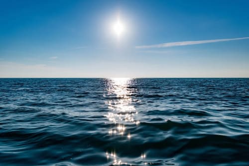 Superficie del océano iluminada por el sol bajo cielo despejado.