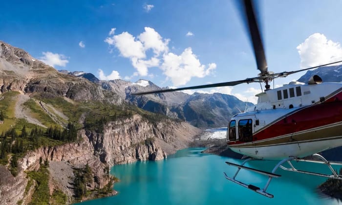 Un helicóptero sobrevuela un lago de agua turquesa rodeado de montañas en una zona remota de Alaska