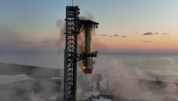 El propulsor Super Heavy desciende sobre la torre de lanzamiento entre humo y llamas durante una maniobra de captura