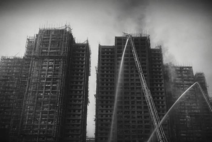 Torres en construcción ennegrecidas mientras bomberos rocían agua tras un incendio de gran magnitud en Hong Kong