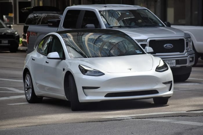 Automóvil Tesla blanco circulando entre otros vehículos en una calle de ciudad