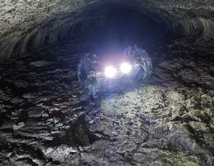 Robot de KAIST avanzando en una cueva de lava mientras ilumina el suelo rocoso con focos frontales