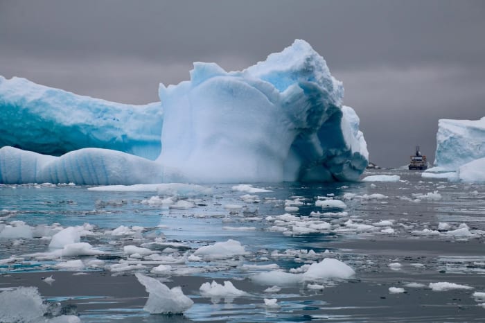 Iceberg en aguas de la Antártida con un barco al fondo