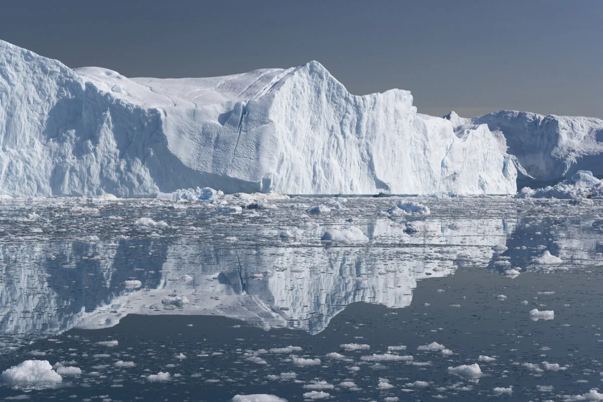 Vista imponente de un glaciar reflejando en el agua, destacando su rol en el ecosistema y como reserva de agua dulce.