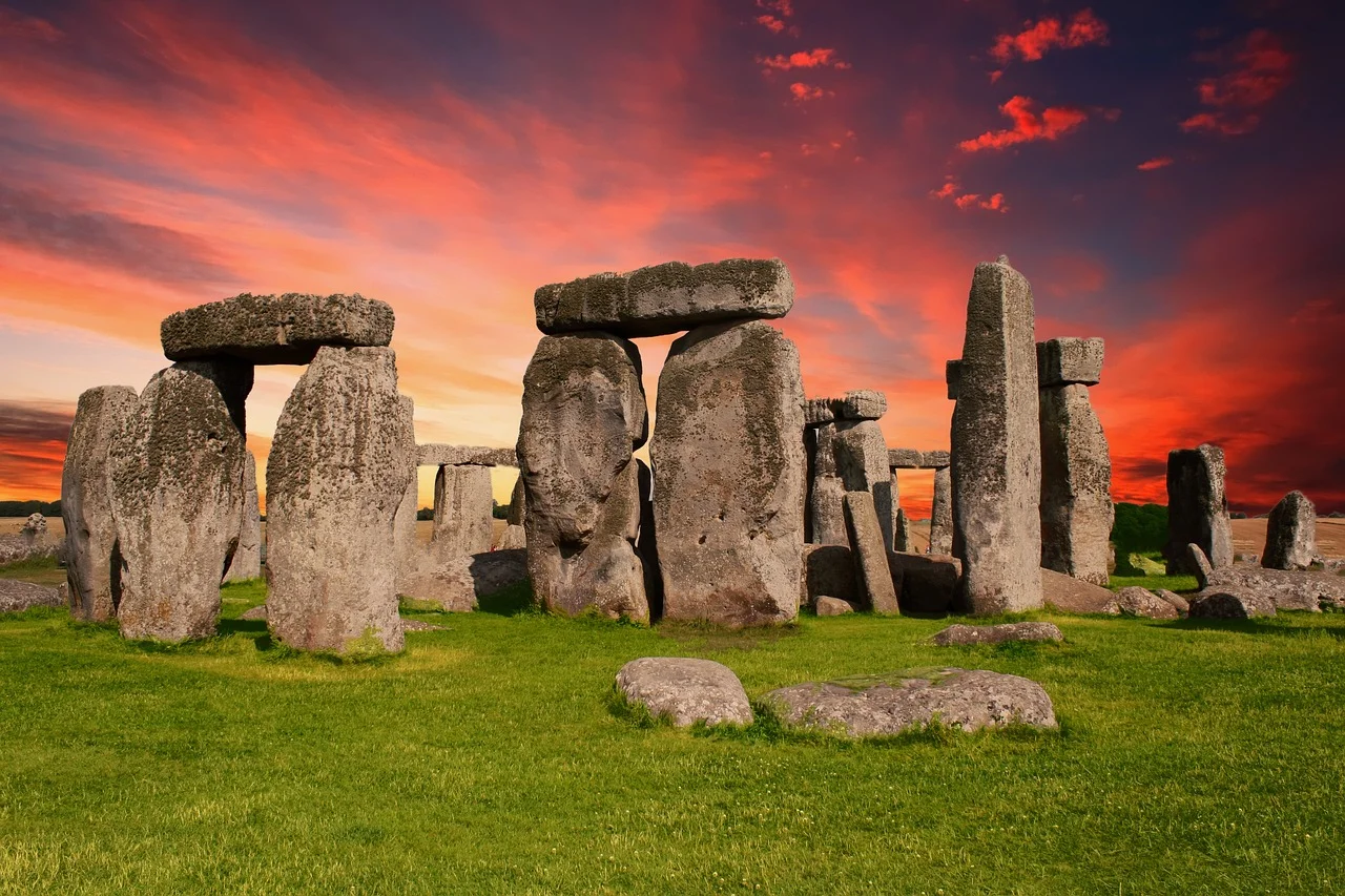 Stonehenge al atardecer con cielo rojizo y nubes, destacando las imponentes estructuras de piedra y el verde pasto de la llanura de Salisbury.