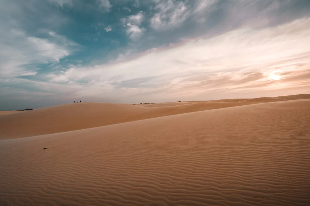 Amanecer sobre dunas del desierto del Sahara con cielo azul parcialmente nublado