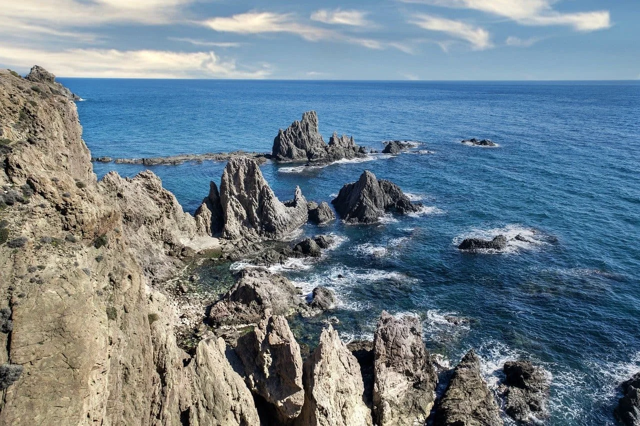 Formaciones rocosas en un arrecife costero junto al océano, con olas rompiendo suavemente y un cielo despejado en el horizonte.
