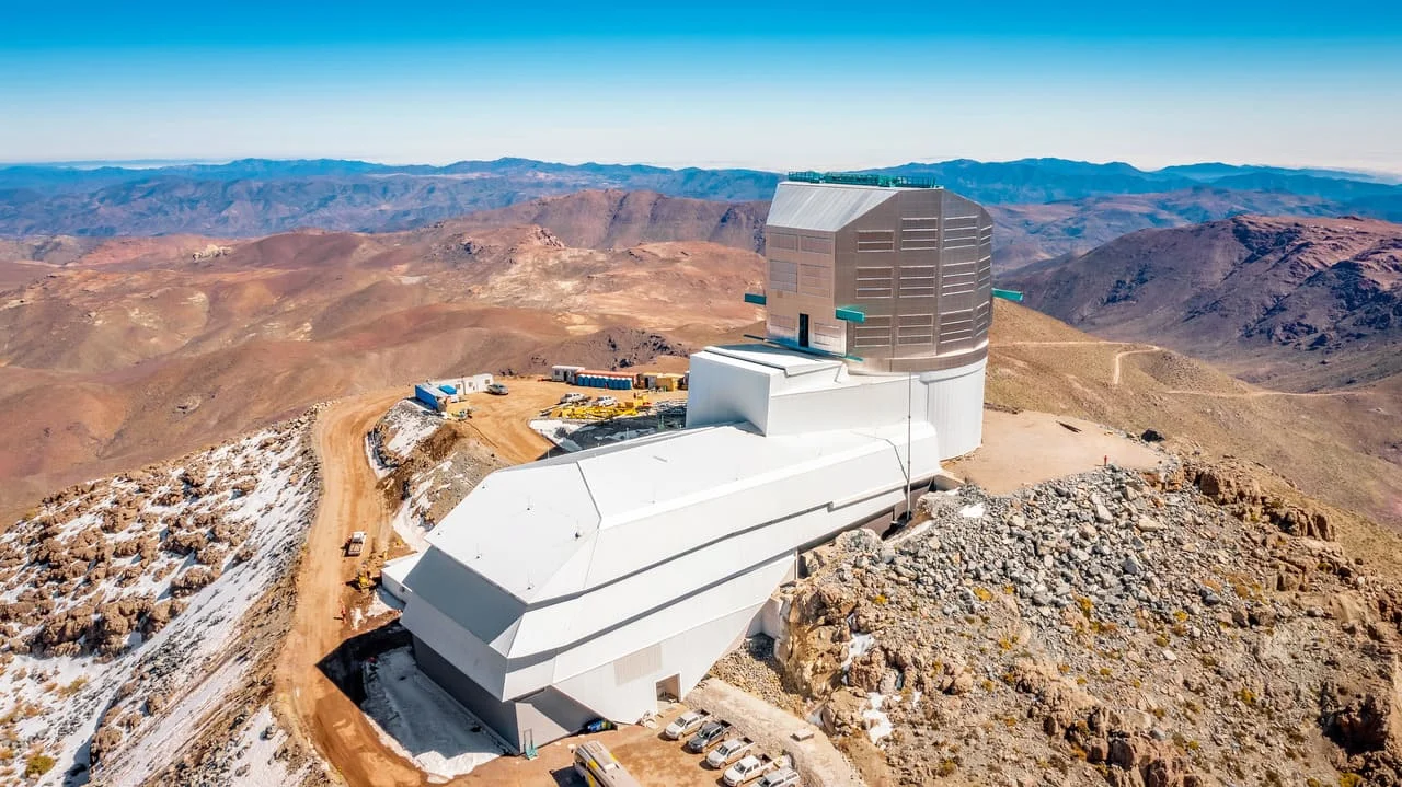 Vista aérea del Observatorio Vera C. Rubin, ubicado en la cima de una montaña rocosa en Chile, rodeado por un paisaje árido y montañoso.