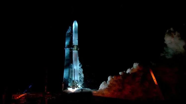 Un cohete New Glenn de Blue Origin en posición vertical, iluminado mientras se prepara para su lanzamiento en un entorno oscuro.