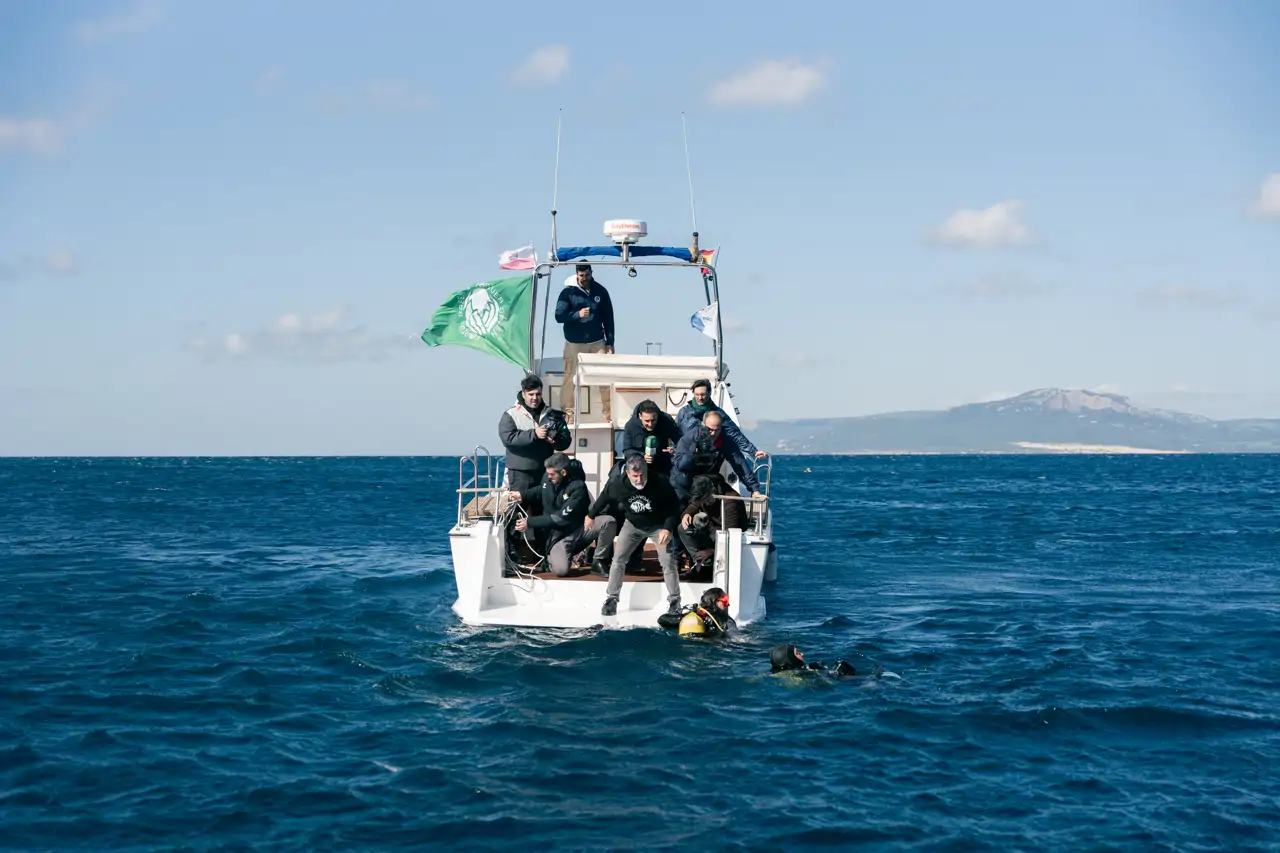 Fotografía de una embarcación con varios tripulantes en el mar, mientras dos buzos nadan cerca.