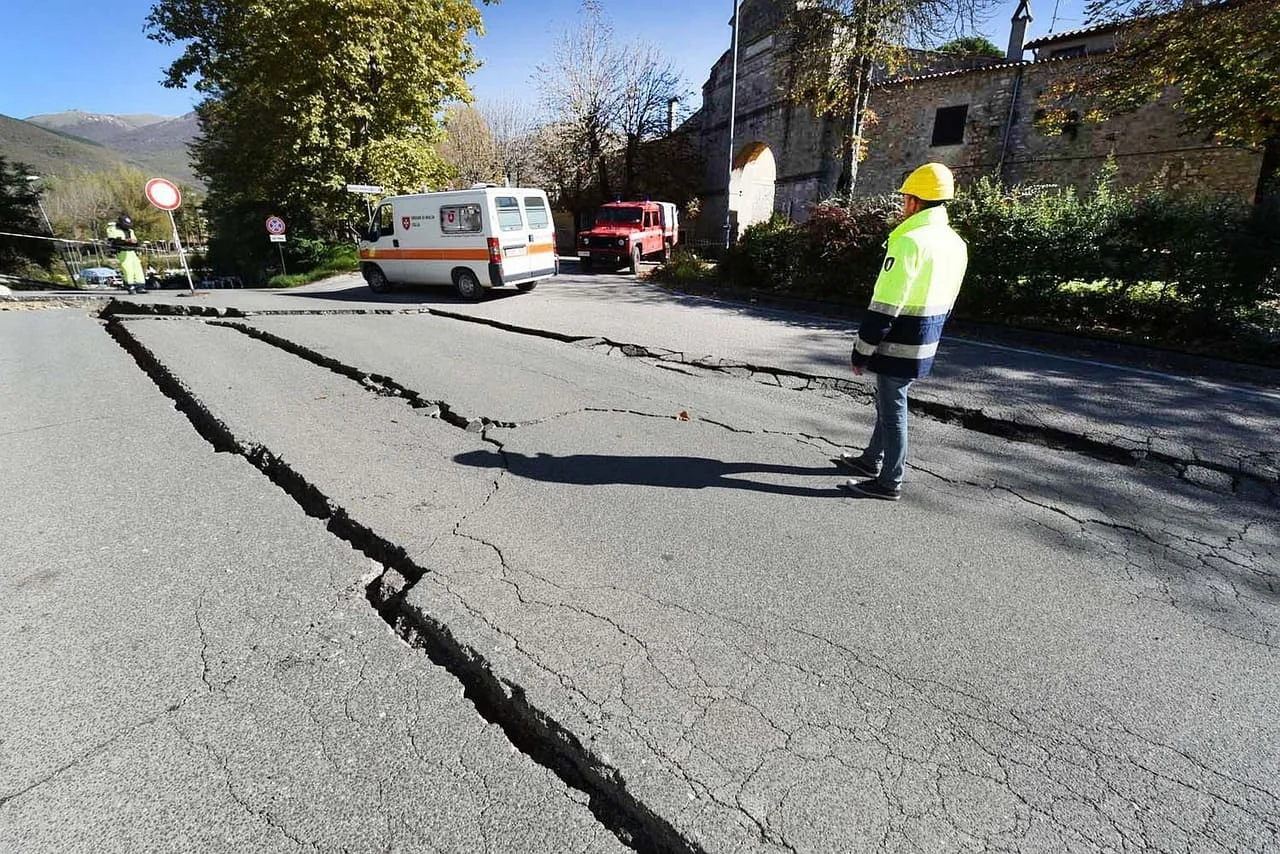 Carretera agrietada tras un terremoto con equipos de emergencia en la escena.