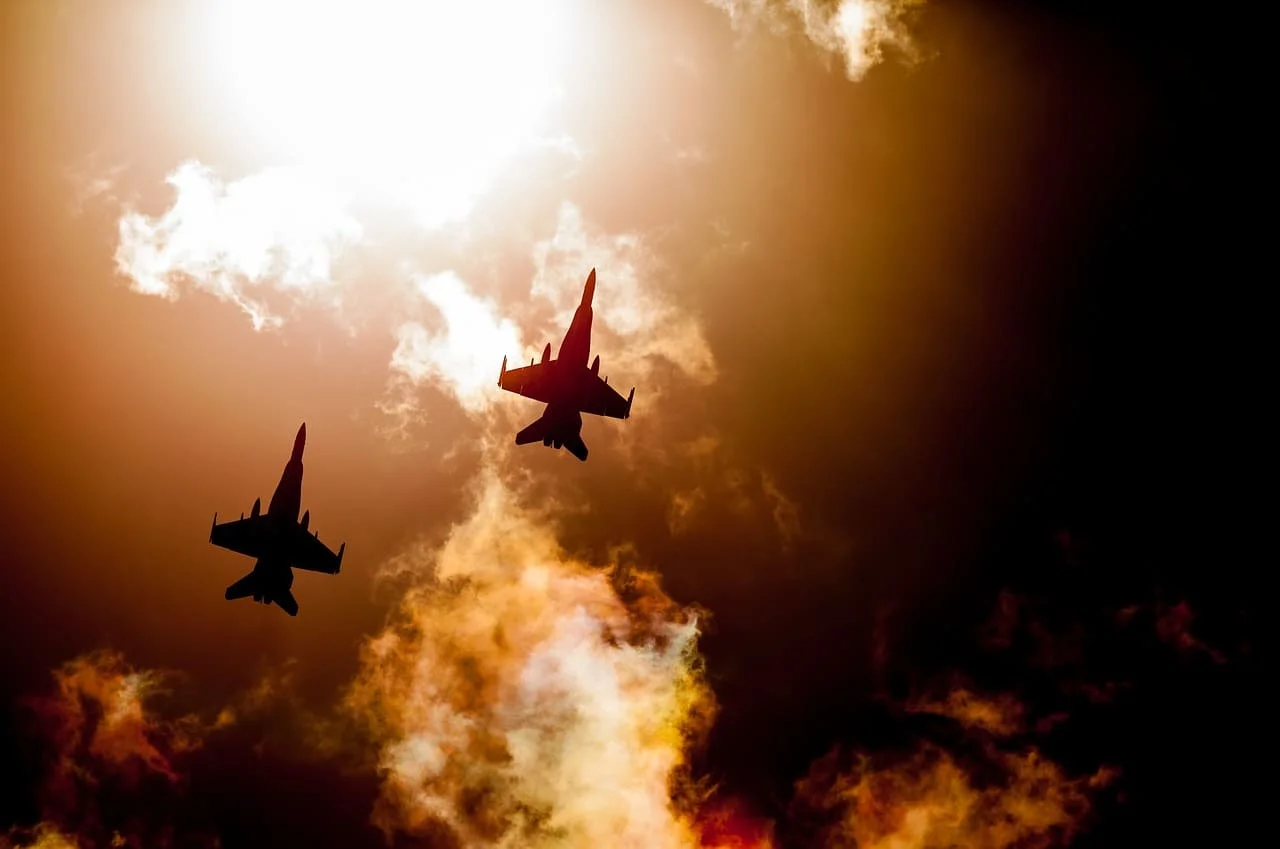 Siluetas de dos aviones militares volando entre nubes y luz solar intensa