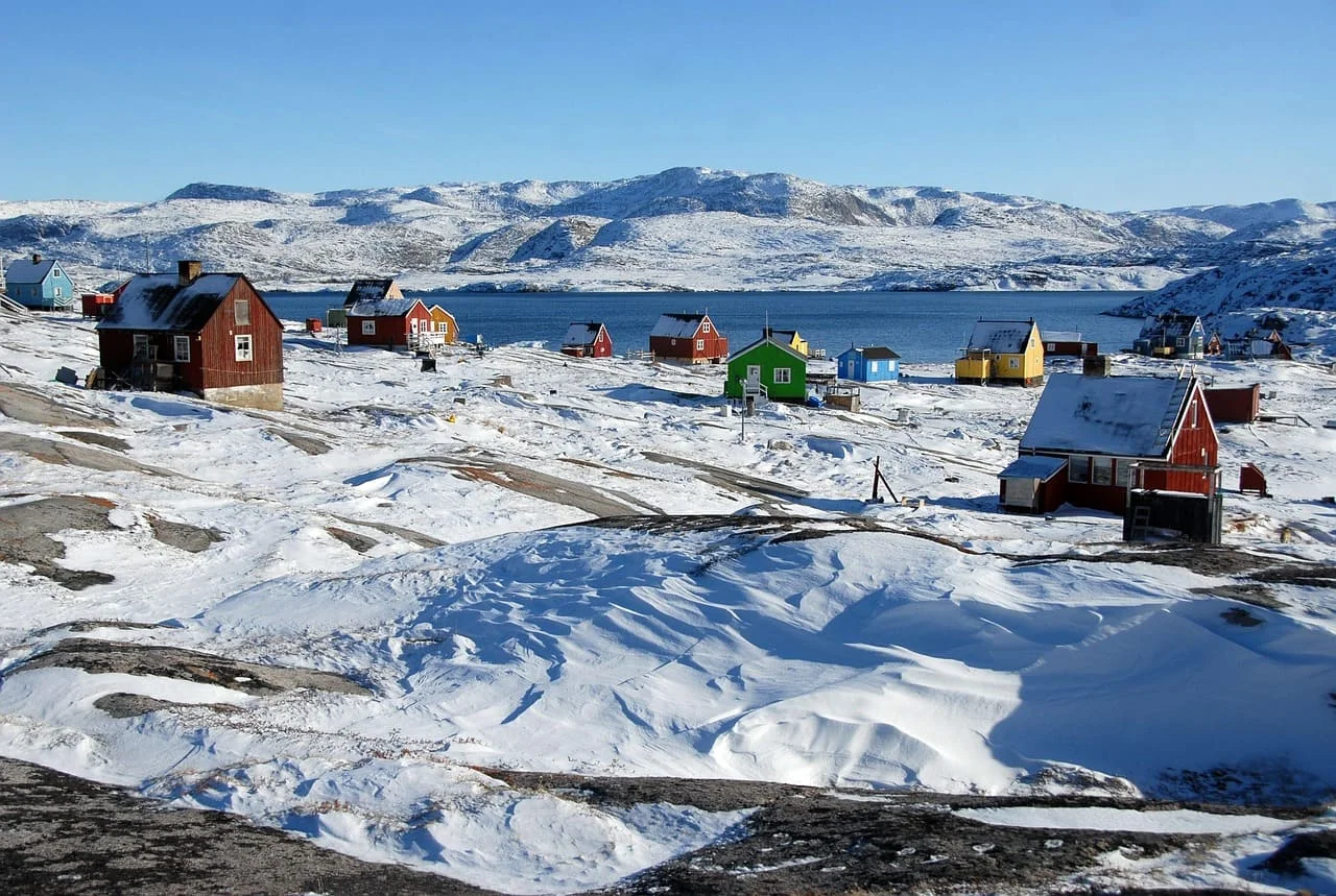Pueblo nevado en Groenlandia con casas de colores junto al mar, en un paisaje ártico.