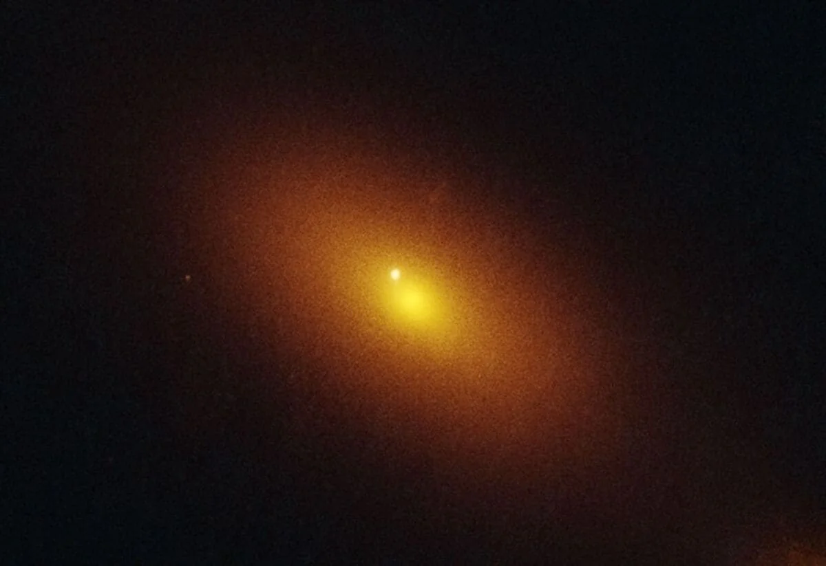 Imagen del Hubble de una galaxia lejana con una nube brillante naranja que marca un agujero negro errante