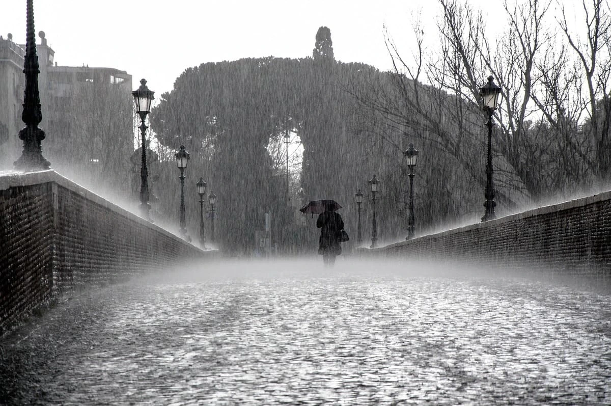 Persona caminando bajo la lluvia en un puente antiguo