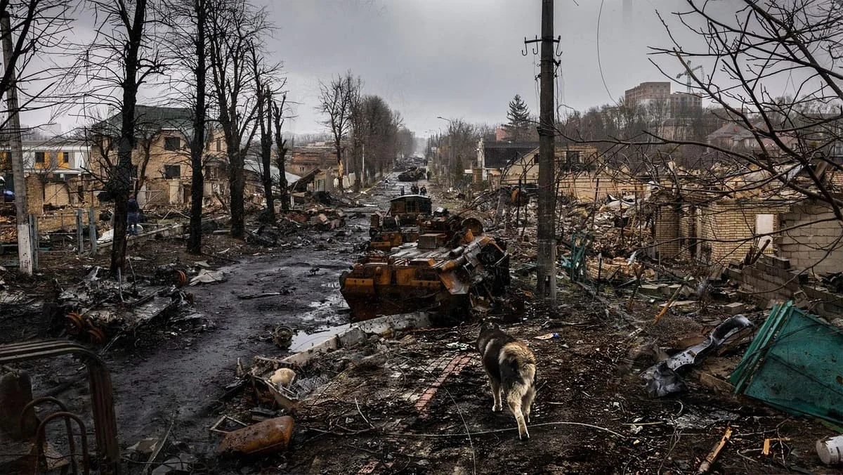 Vista de una ciudad devastada por la guerra, con vehículos destruidos y calles cubiertas de escombros