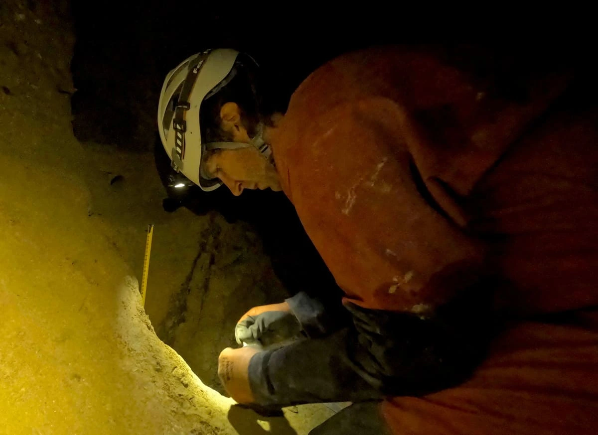 Científico con casco inspeccionando muestras de sedimento en una cueva húmeda y oscura