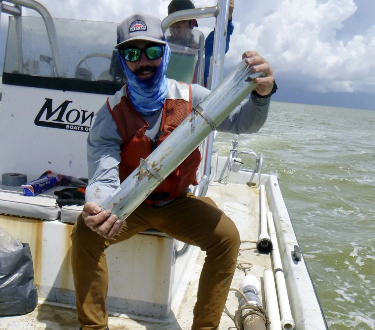 Investigador en una embarcación sosteniendo un tubo con muestras de sedimento marino extraído de la bahía