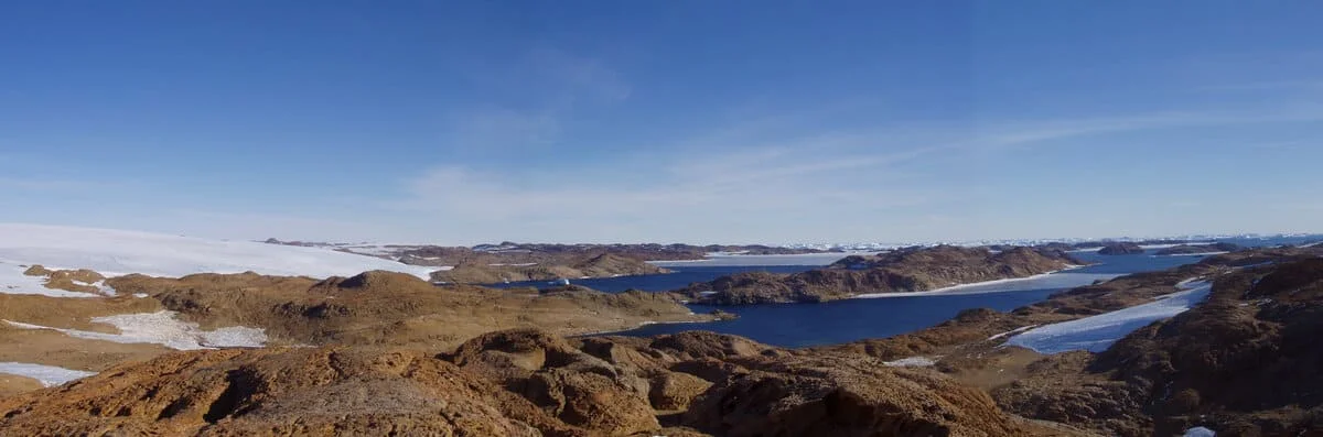 Vista panorámica de colinas, glaciares y lagos en la Antártida Oriental bajo el cielo azul.