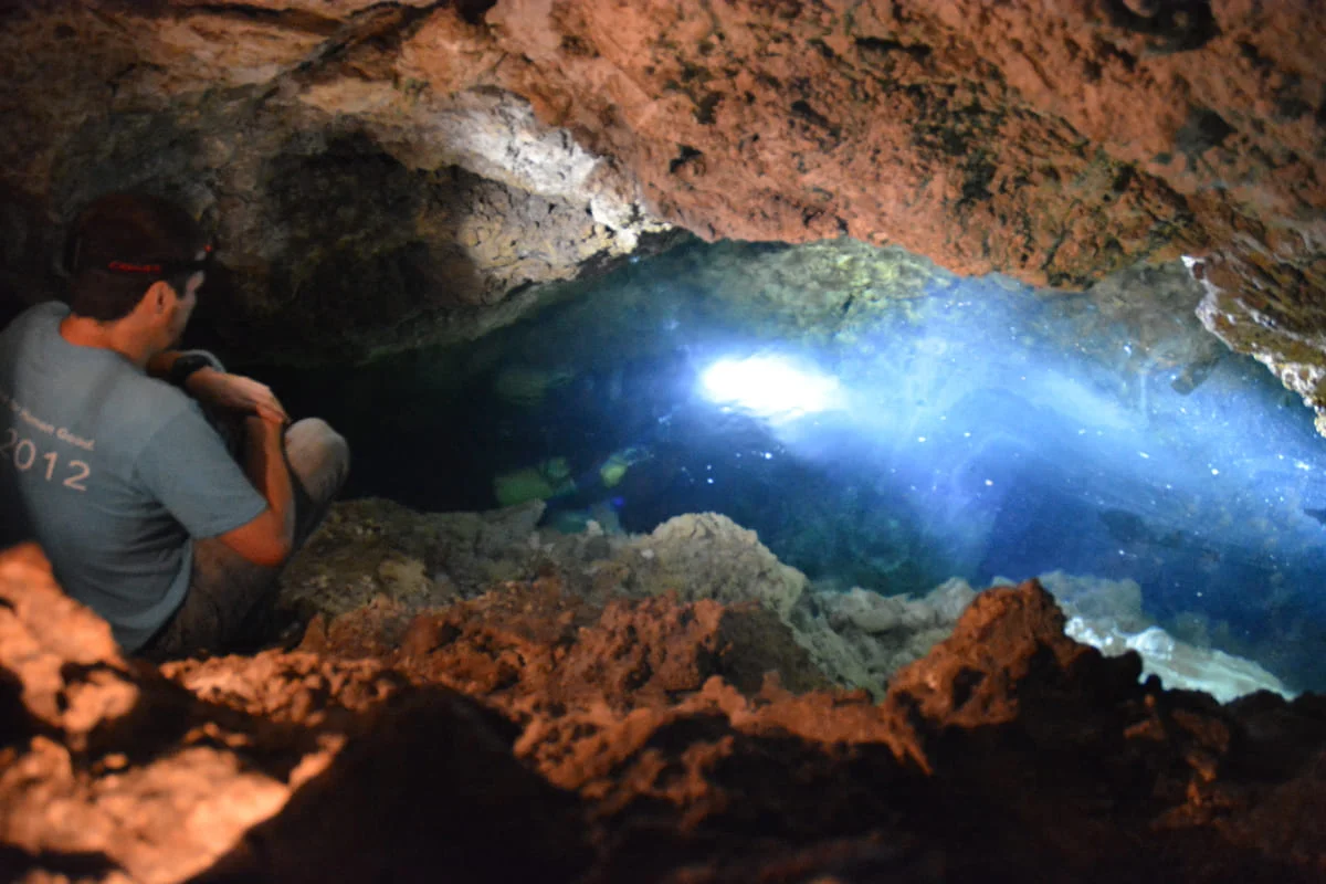 Equipo de científicos observando un pozo de agua subterránea iluminado dentro de la cueva Roadside