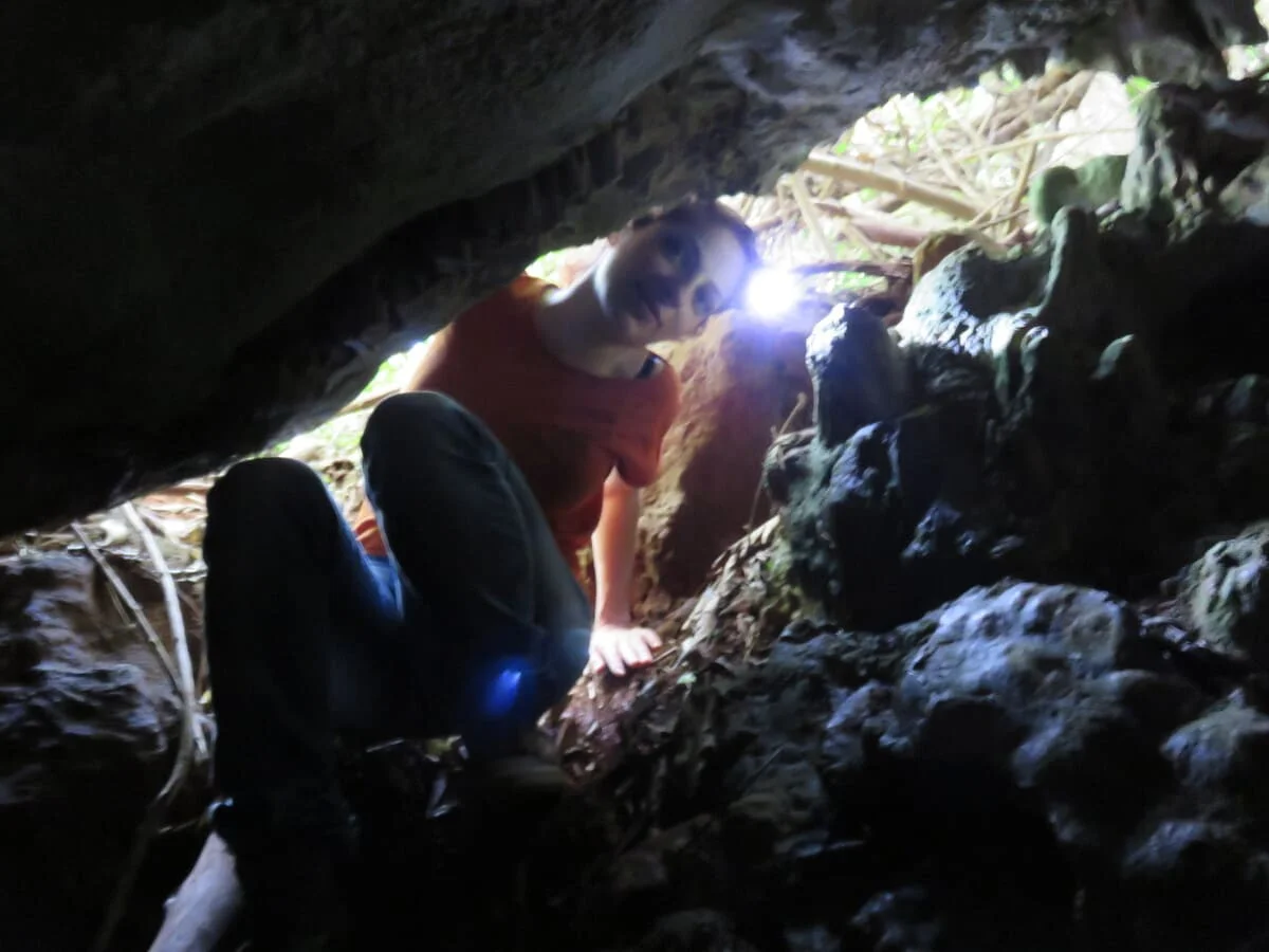 Investigadora accediendo a la cueva Roadside con frontal luminoso, rodeada de rocas y vegetación