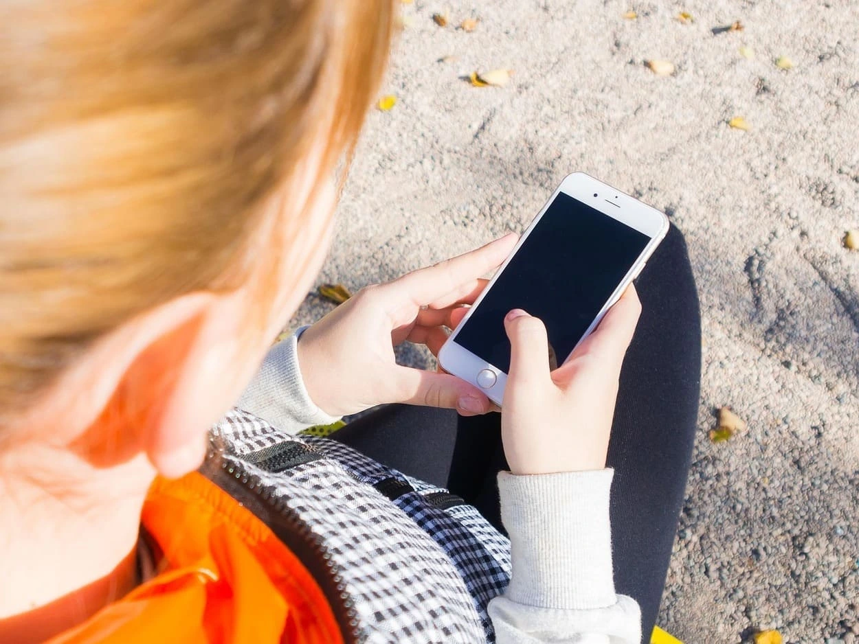 Persona joven sostiene un smartphone mientras revisa la pantalla sentada al aire libre