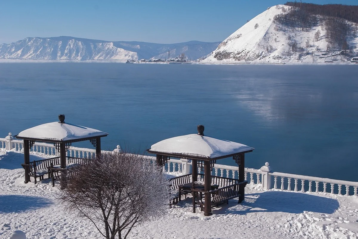 Lago Baikal, orilla cubierta de nieve con pérgolas de madera, aguas azules y montañas en el horizonte.