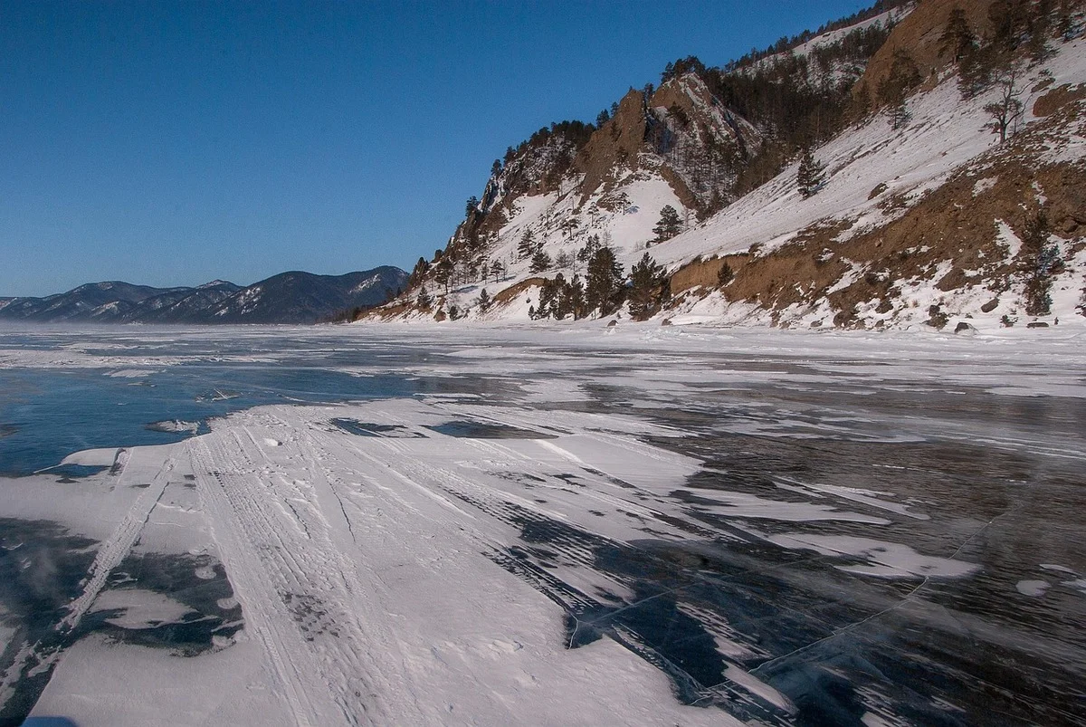 Lago Baikal congelado, nieve sobre el hielo y montañas al fondo bajo el cielo azul.