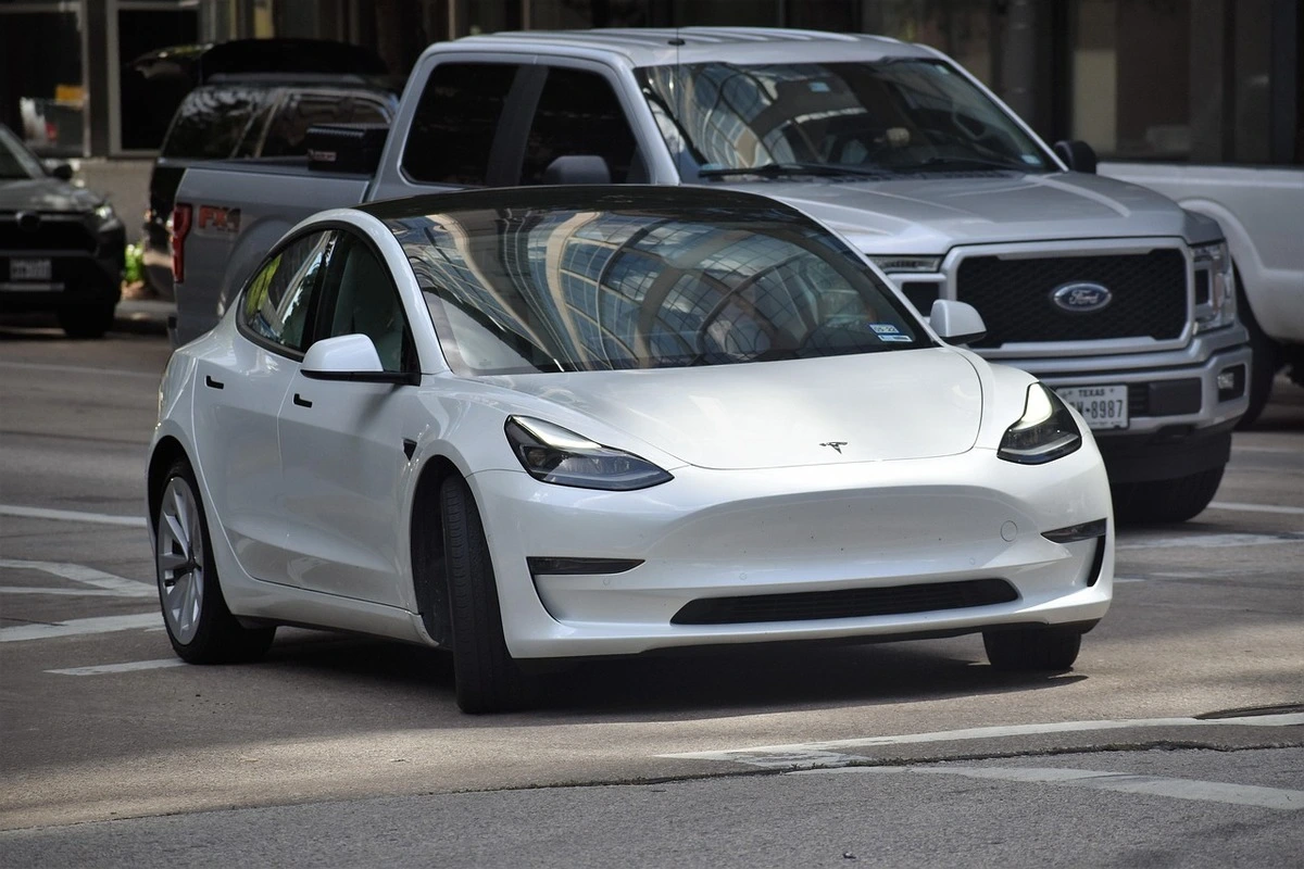 Automóvil Tesla blanco circulando por una avenida en entorno urbano moderno