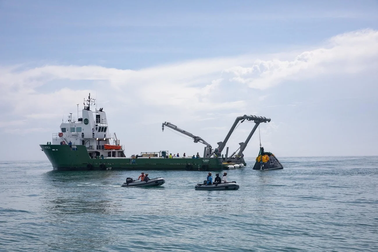 Barco de recuperación de la NASA y embarcaciones auxiliares trabajando para recuperar una cápsula espacial durante pruebas en el océano.