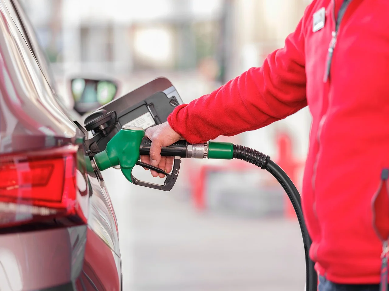 Empleado de gasolinera con chaqueta roja llenando el depósito de un automóvil