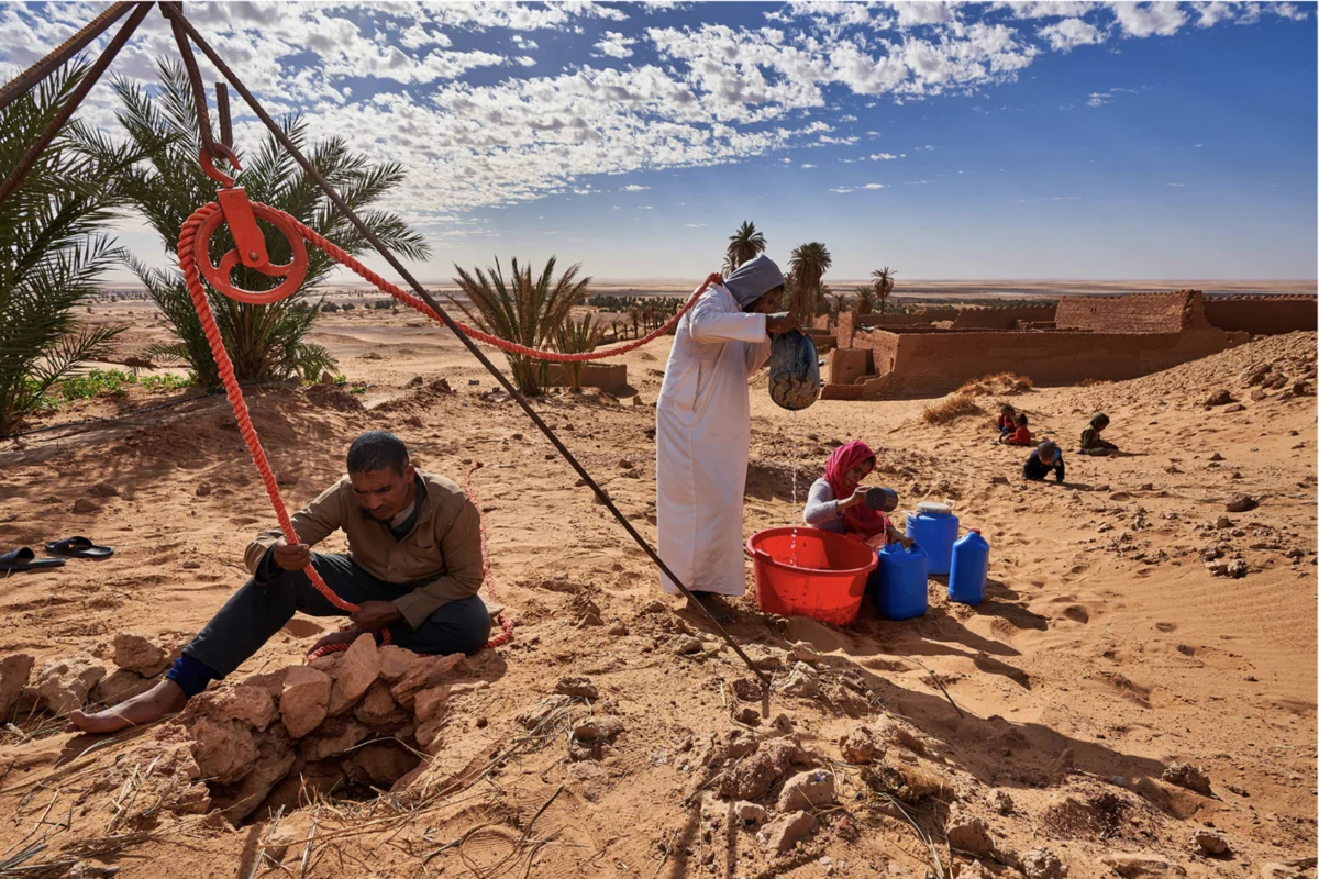 Personas extrayendo agua de un pozo en el desierto con sistema de poleas manual