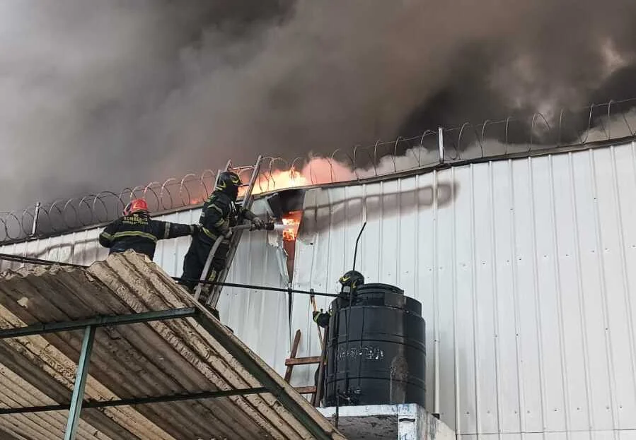 Bomberos trabajan en el techo de una vivienda para sofocar las llamas que emergen entre las láminas y el humo espeso