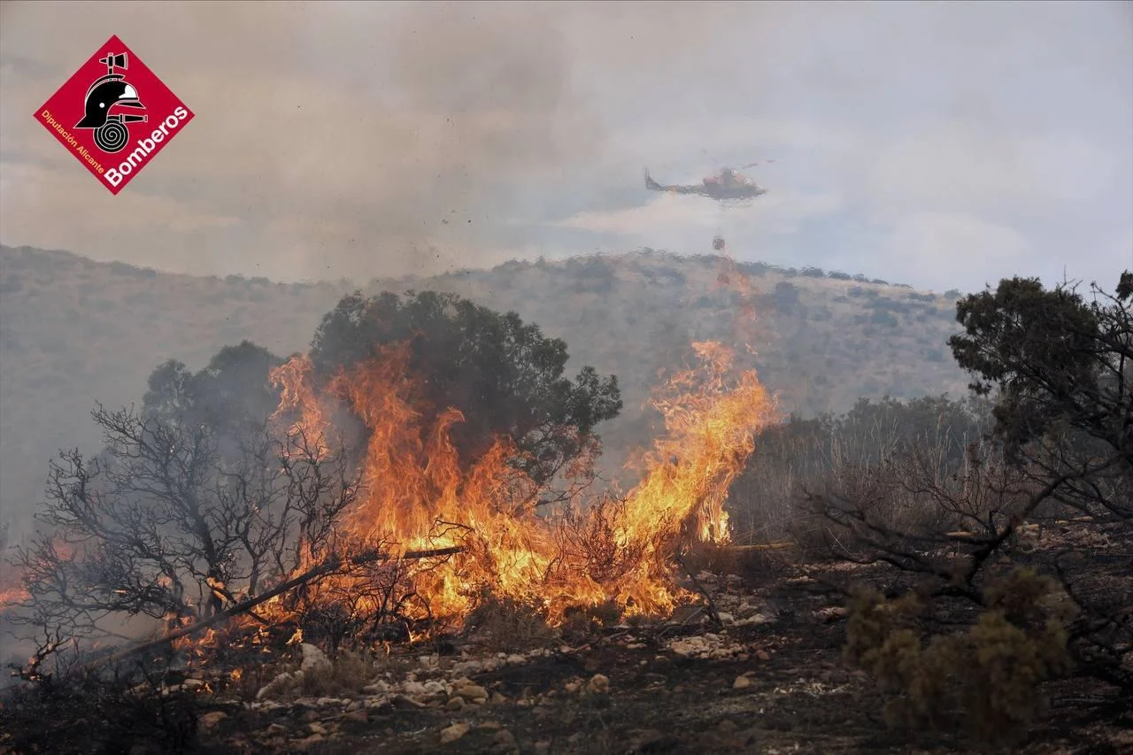 Incendio forestal activo en zona montañosa de Ibi, con llamas intensas y helicóptero de extinción sobrevolando