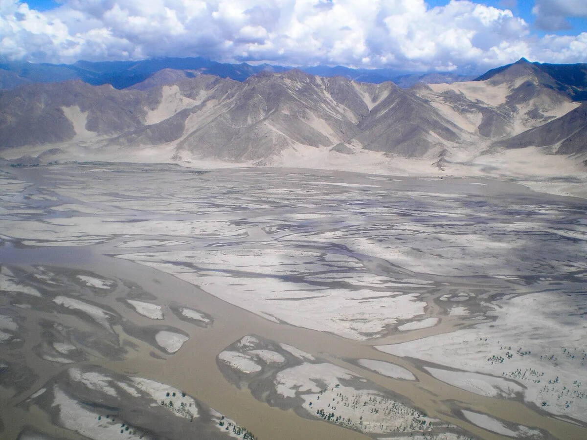 Vista panorámica del río Yarlung en el Tíbet, rodeado de montañas y vegetación, bajo un cielo despejado