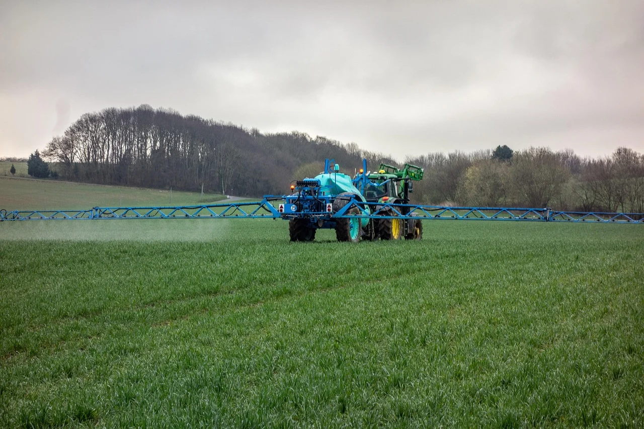 Tractor agrícola aplicando fertilizante líquido en un campo verde, con árboles al fondo y cielo nublado