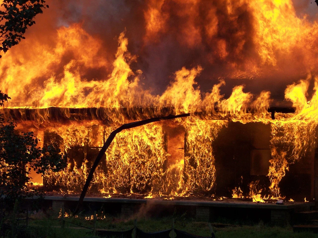 Incendio destruyendo una estructura de madera, con intensas llamas y humo denso