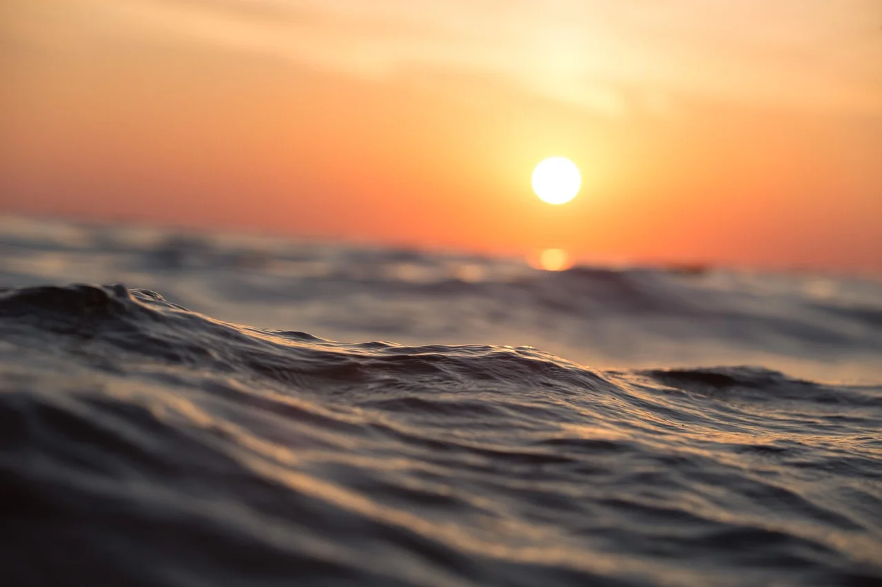 Primer plano de las olas del océano al amanecer, con el sol elevándose en el horizonte y un cielo anaranjado