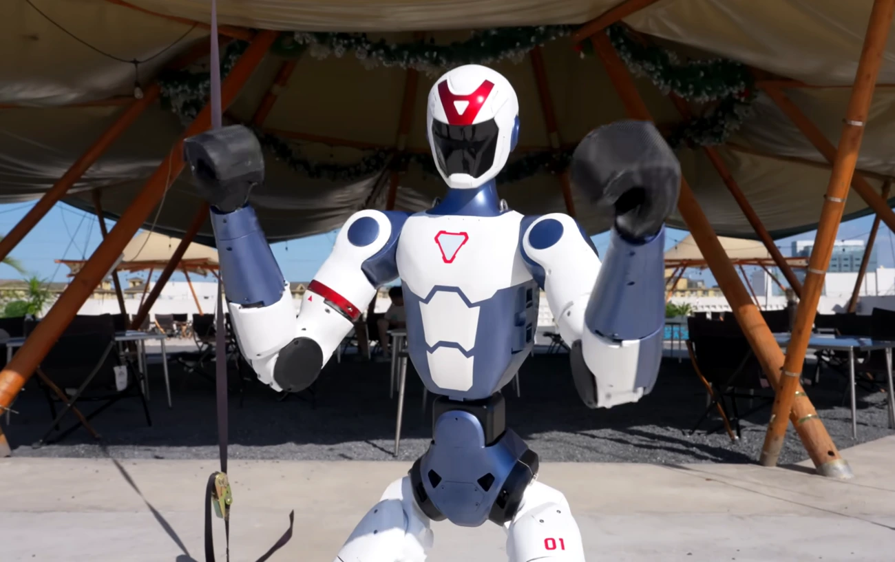 Robot humanoide Unitree R1 realizando movimientos acrobáticos al aire libre, bajo una carpa de madera