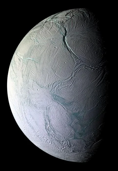 La luna Encélado de Saturno, cubierta de hielo y con fracturas visibles, flotando en el espacio oscuro.