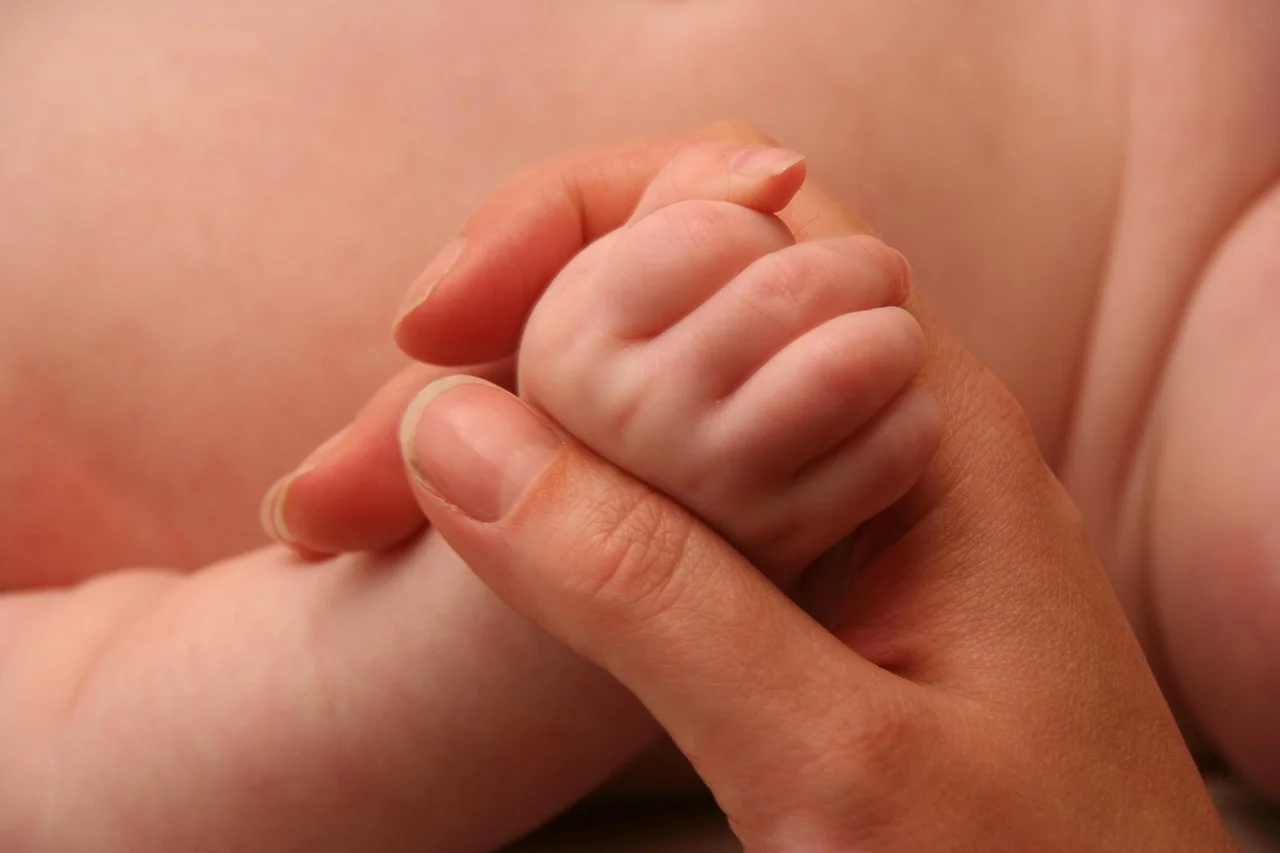Mano de un adulto sosteniendo con delicadeza la mano de un bebé