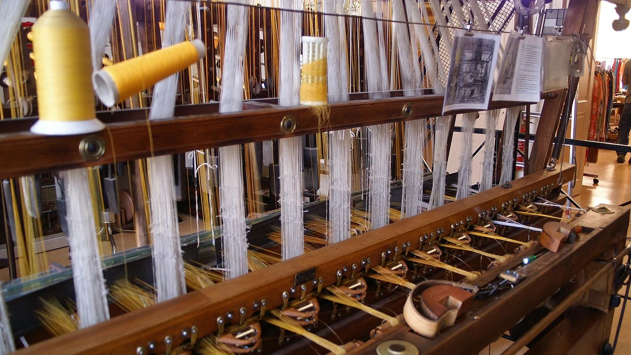 Telar mecánico de una fábrica de seda con bobinas de hilo amarillo y blanco, mostrando el proceso industrial de tejido