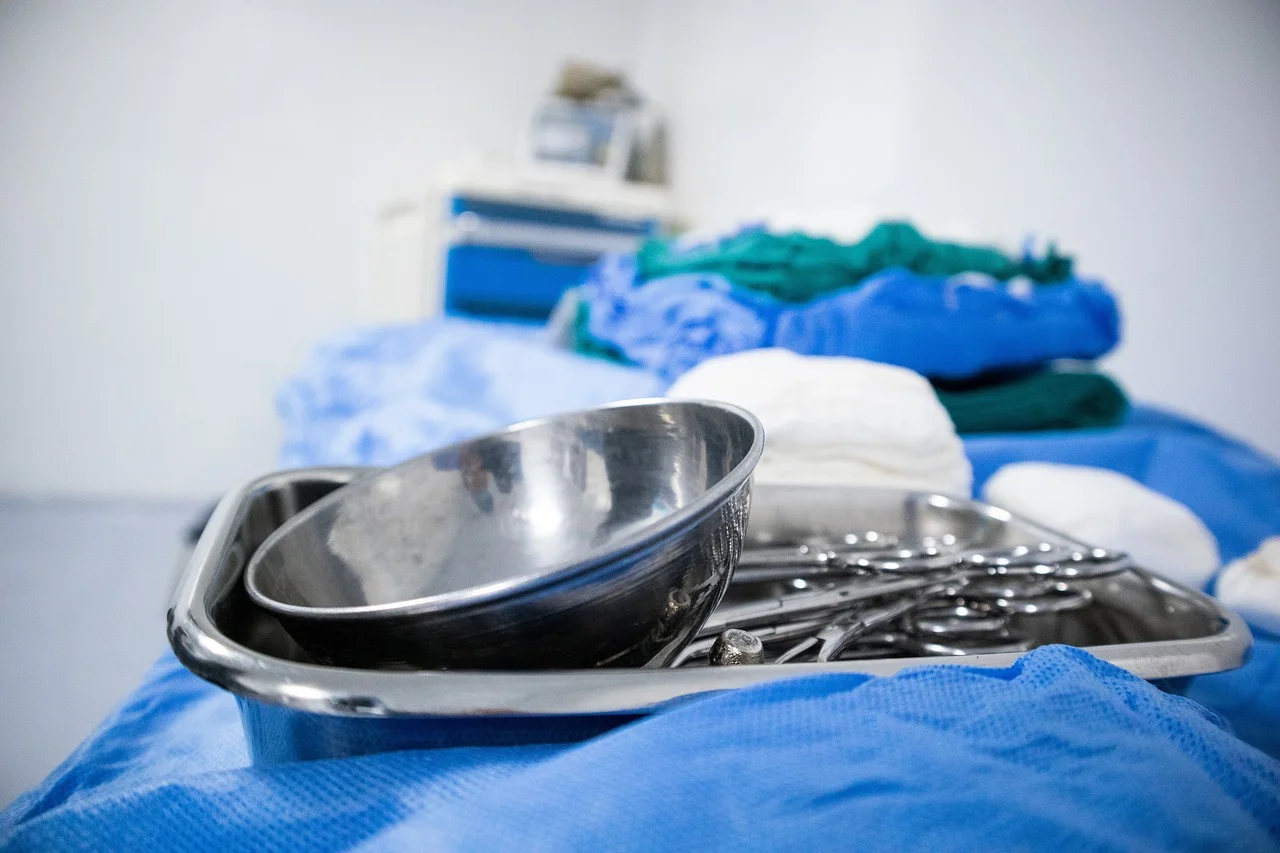 Bandeja con instrumental quirúrgico de acero inoxidable en un quirófano, sobre sábanas azules estériles y textiles médicos apilados al fondo