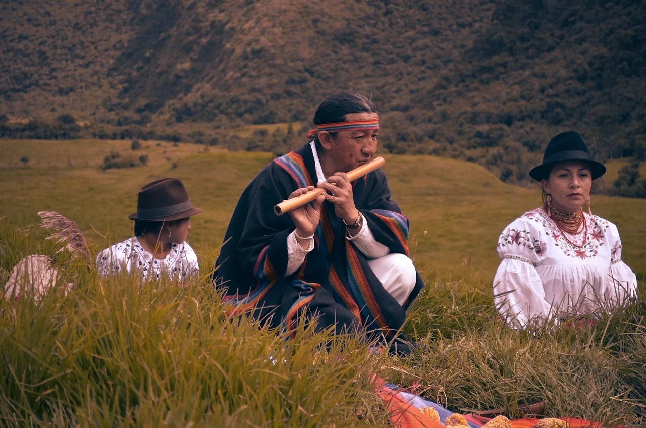 Persona indígena con vestimenta tradicional andina tocando la flauta en un entorno natural
