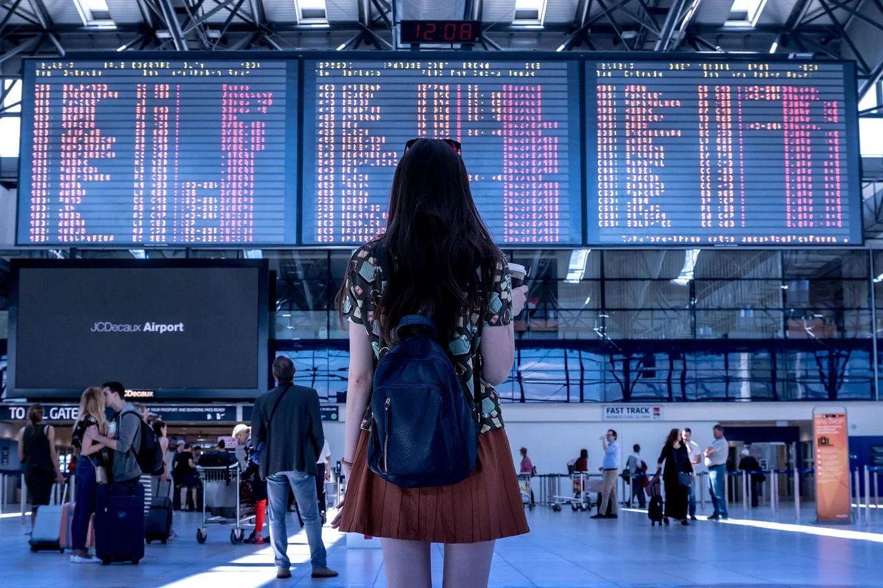 Joven con mochila de espaldas observa los paneles de salidas de vuelos en un aeropuerto