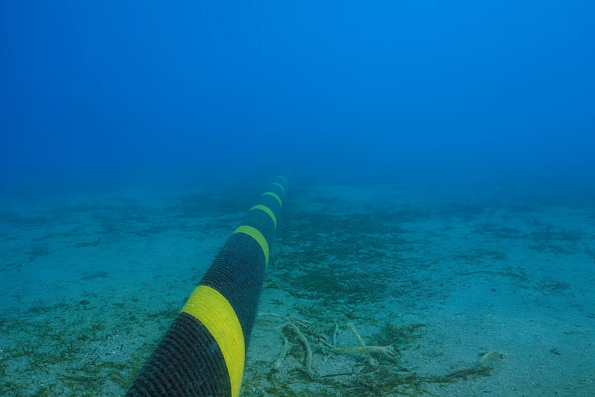 Vista submarina de un cable de comunicaciones tendido sobre el lecho marino con agua de tono azul profundo