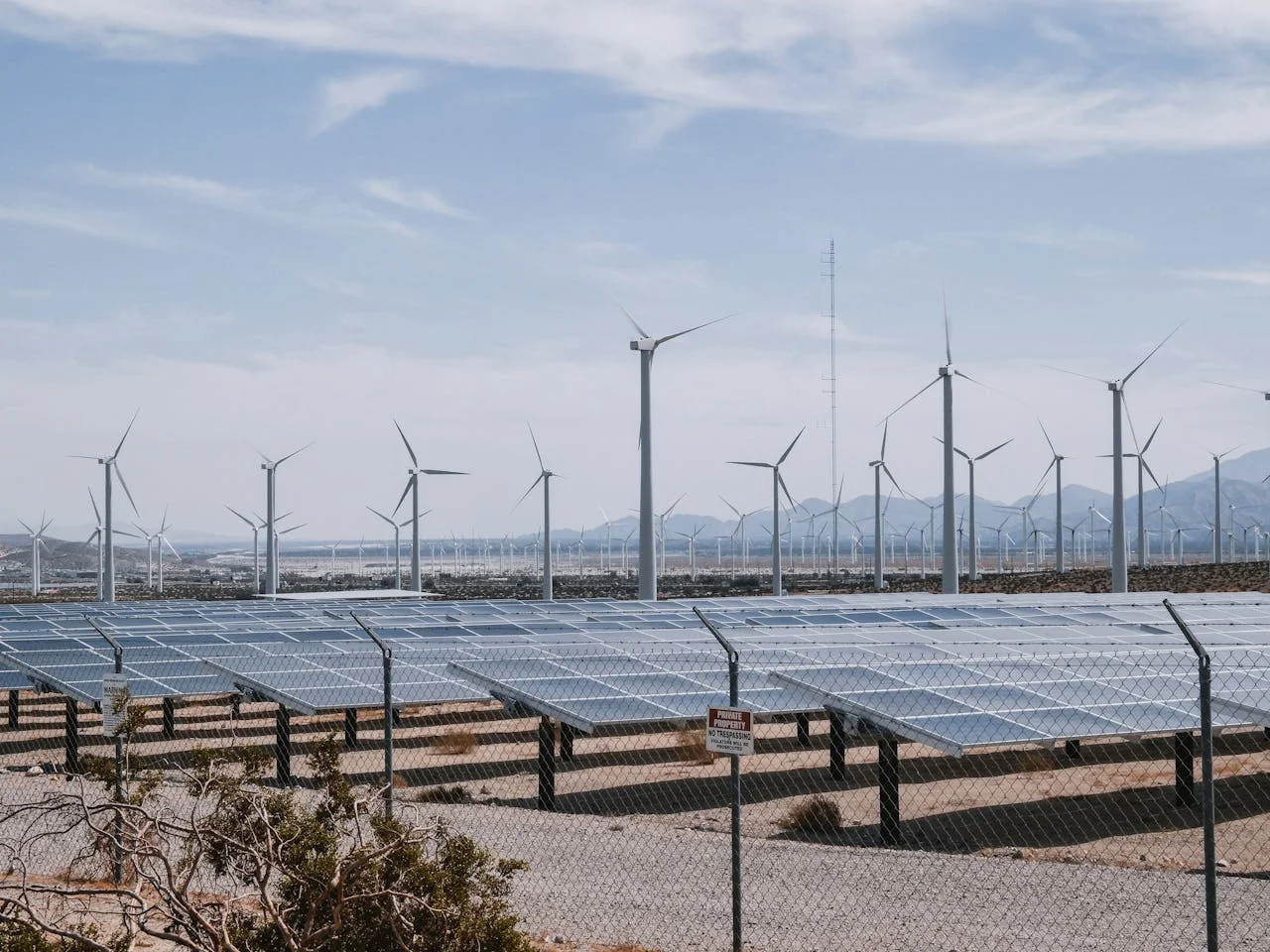 Plantas solares y parque eólico en un paisaje desértico con montañas al fondo