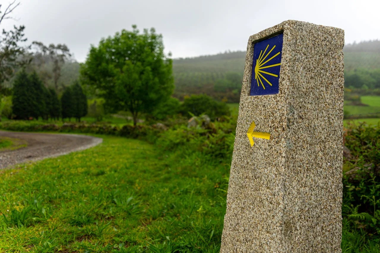 Mojón de granito con la concha amarilla, símbolo del Camino de Santiago, en un sendero rural de Galicia