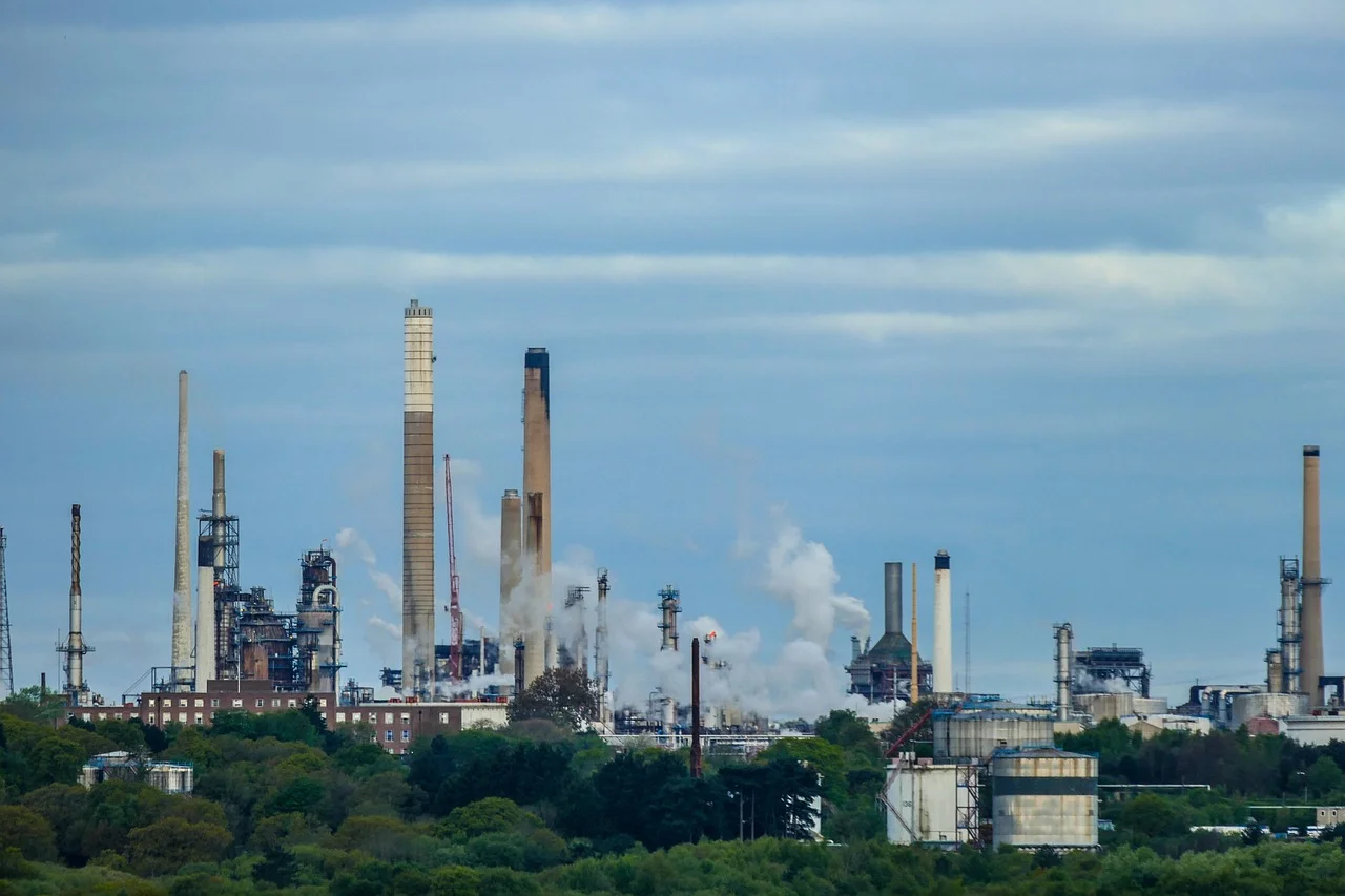 Vista panorámica de una refinería de petróleo con chimeneas expulsando humo y tanques de almacenamiento